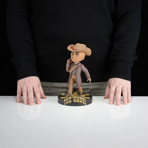 A tan cowboy-themed bobblehead figurine with a brown hat and gray coat, standing on a black base engraved with ’the ghoul’ in gold lettering.
