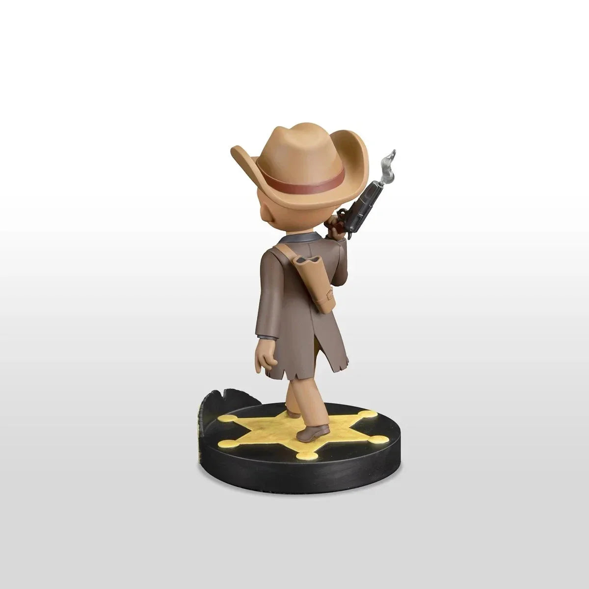 A tan cowboy figurine with a brown hat and coat, holding a smoking revolver, stands on a black circular base featuring a yellow star.