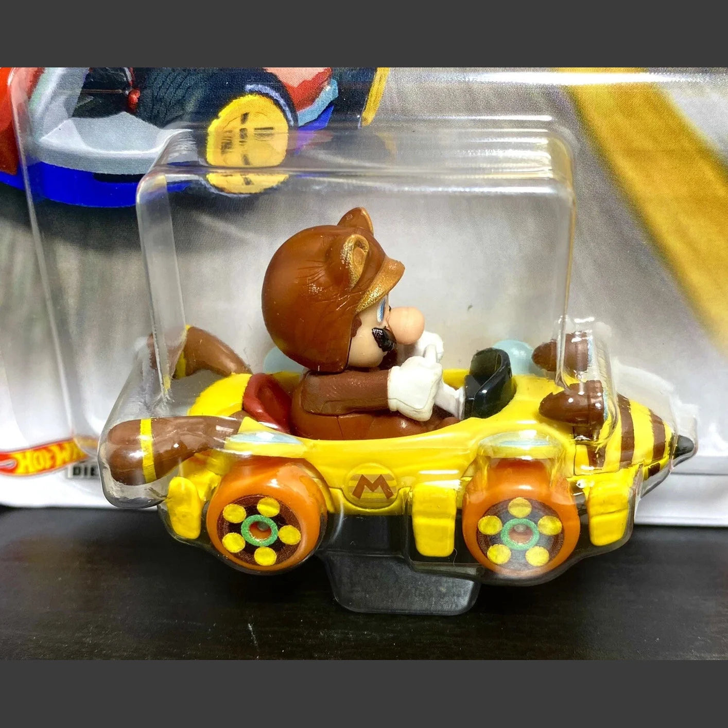 Yellow and brown teddy bear in a car toy with clear plastic packaging.