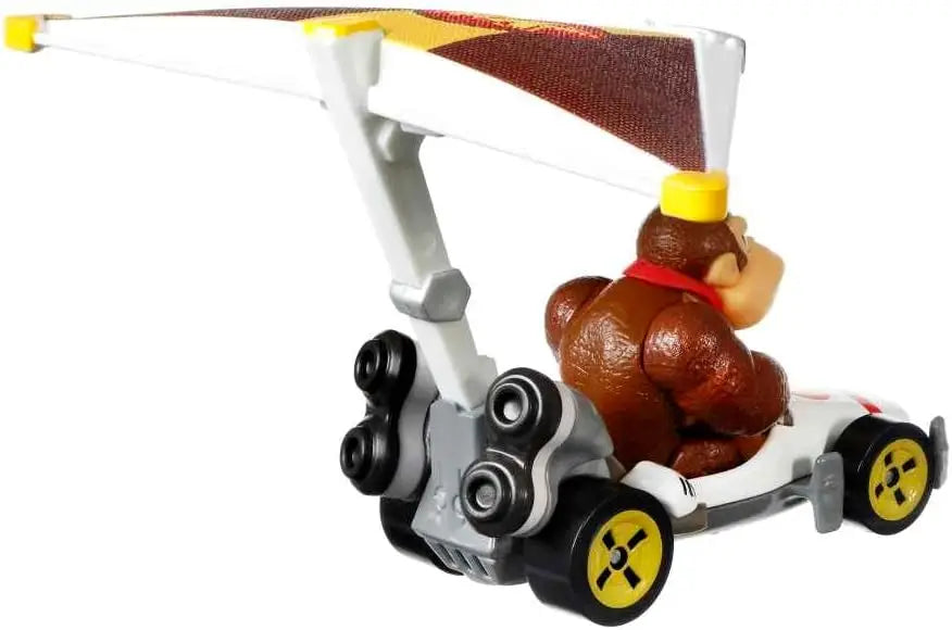 Brown donkey kong figure seated in white and gray hot wheels mario kart b-dasher race car with yellow radioactive wheels
