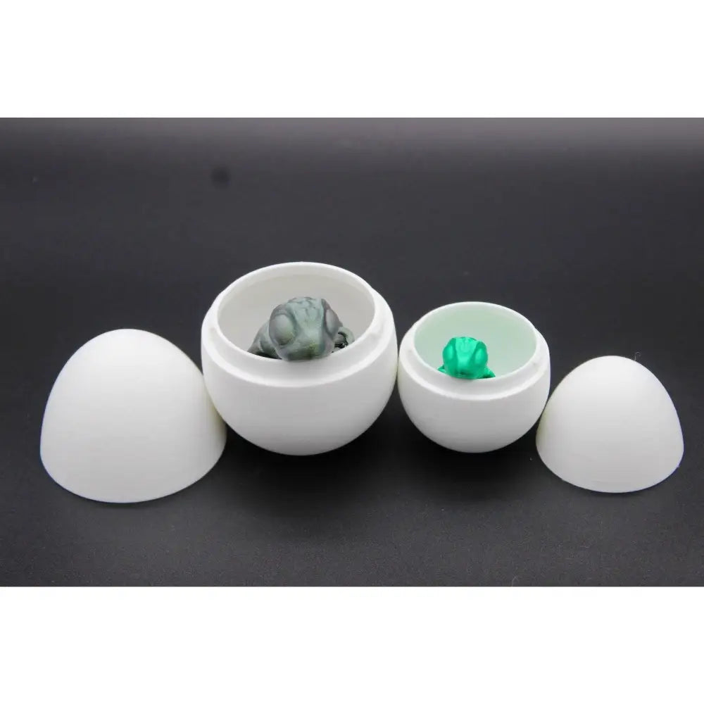 Two white egg-shaped containers with small frog figurines.