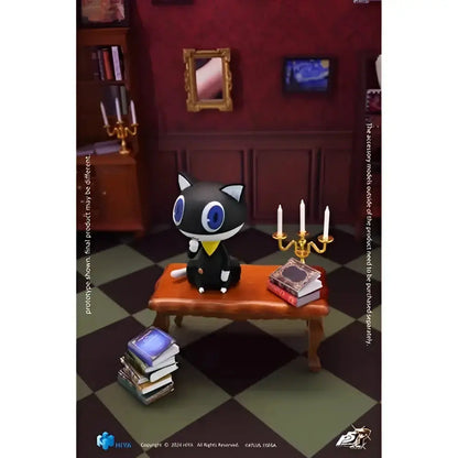 A black cat figurine with blue eyes and yellow collar sitting on an orange bench in persona 5 royal joker action figure