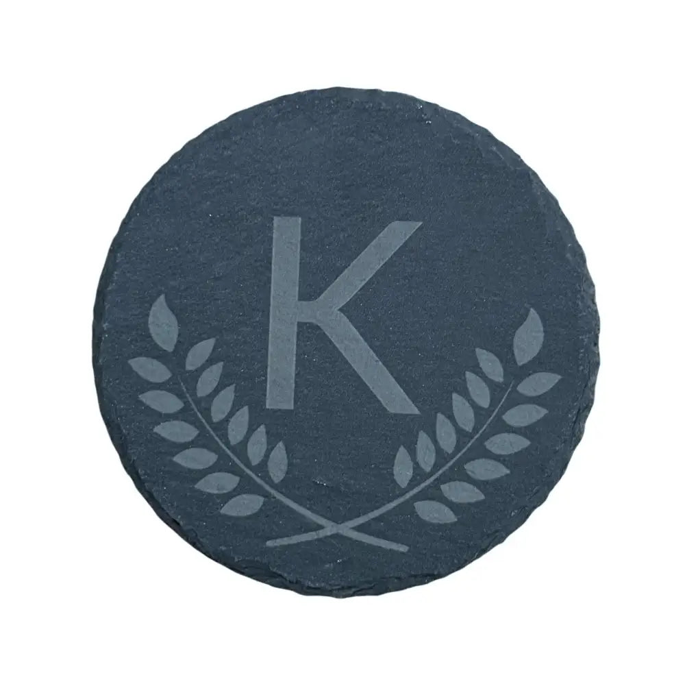 Round slate coaster with an etched ’K’ and laurel wreath design.