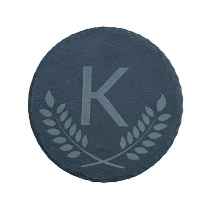 Round slate coaster with an etched ’K’ and laurel wreath design.