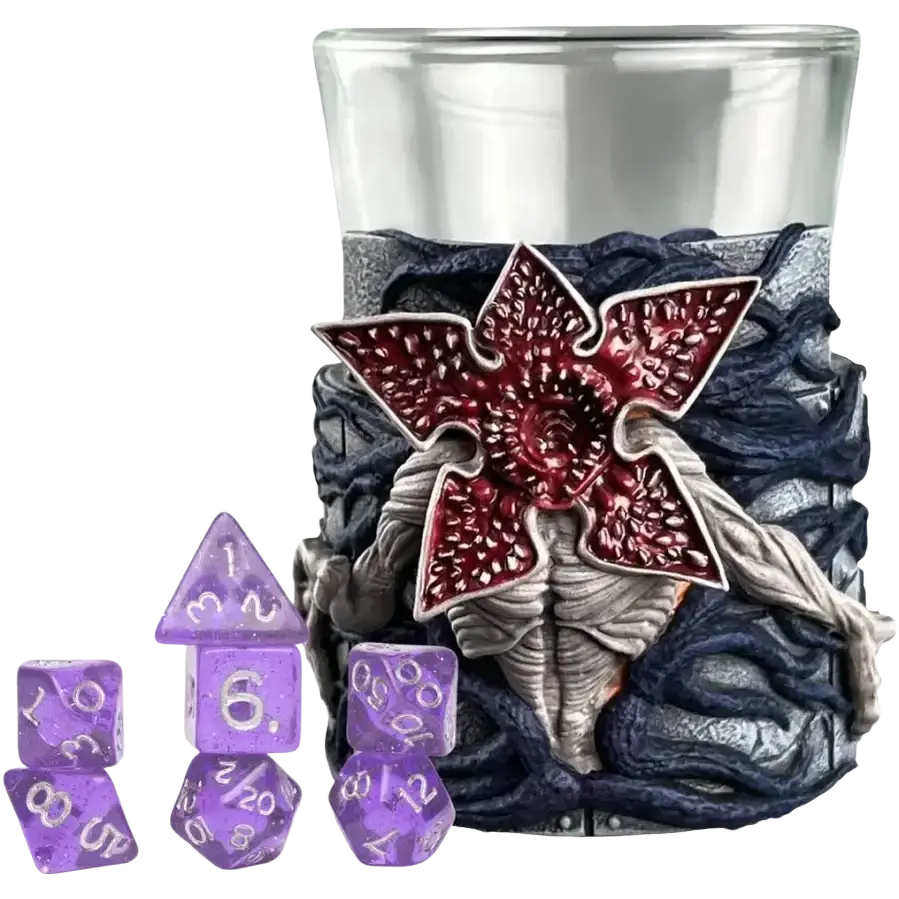 Purple glittery polyhedral dice set with a clear glass tumbler wrapped in textured gray and navy material featuring a red, detailed monster emblem.